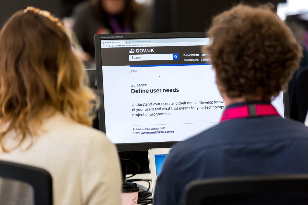 Two people from the Technology Policy team looking at a computer screen containing the words "Define user needs. Understand your users and their needs. Develop knowledge of your users and what that means for your technology project or programme."