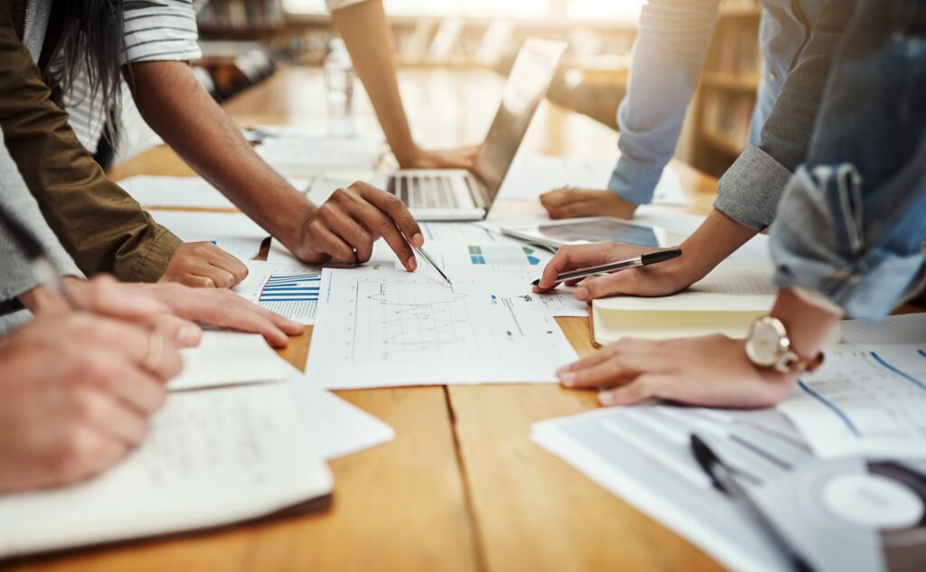 Photo of people in meeting around a table demonstrating collaboration and paperwork with hand gestures